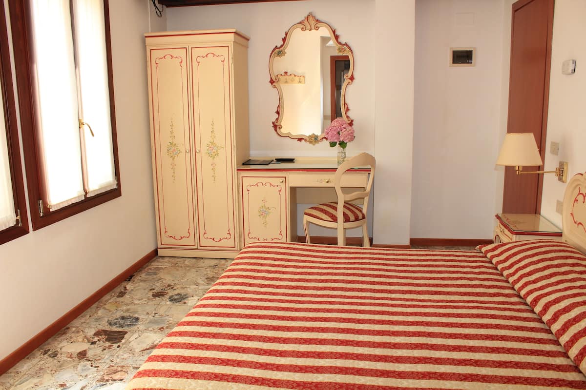 A bedroom with a bed, a desk, a chair, a mirror, and a wardrobe.
