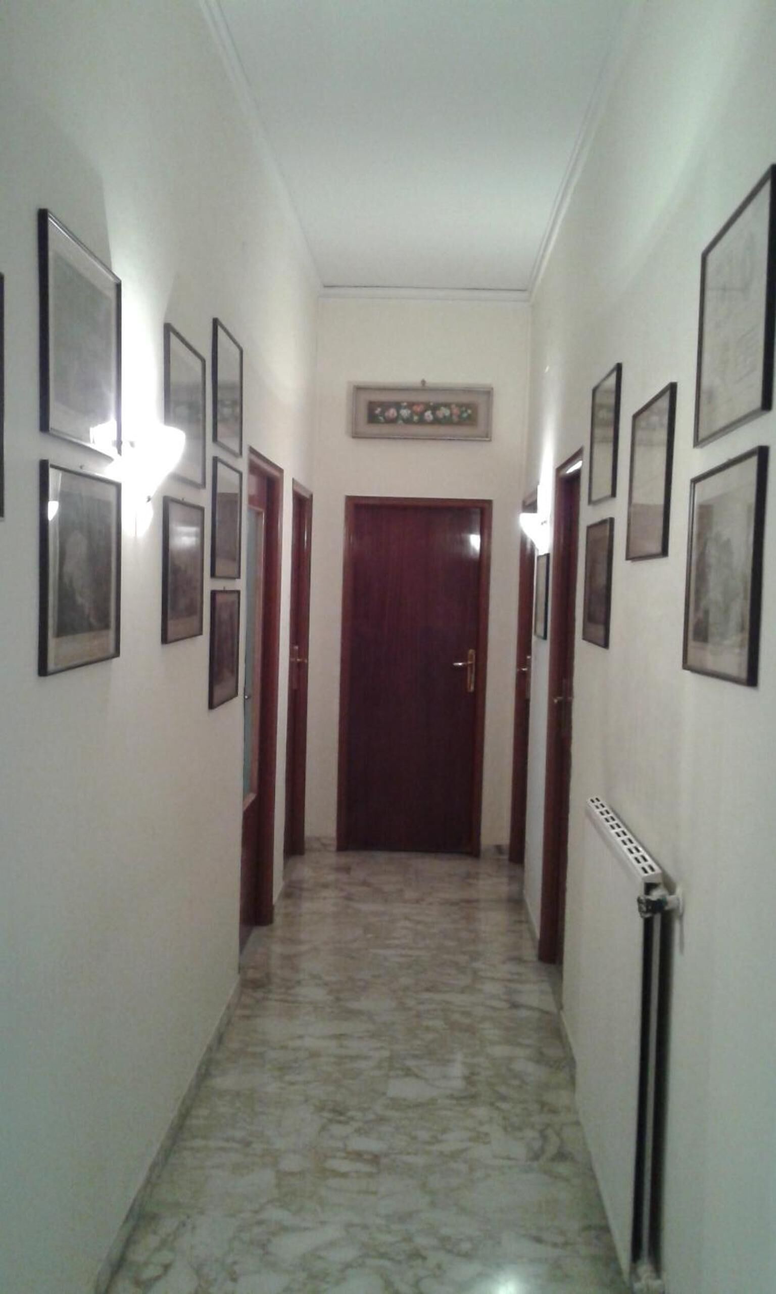 Un pasillo con cuadros enmarcados en las paredes, una puerta de madera al final y un radiador a la derecha.