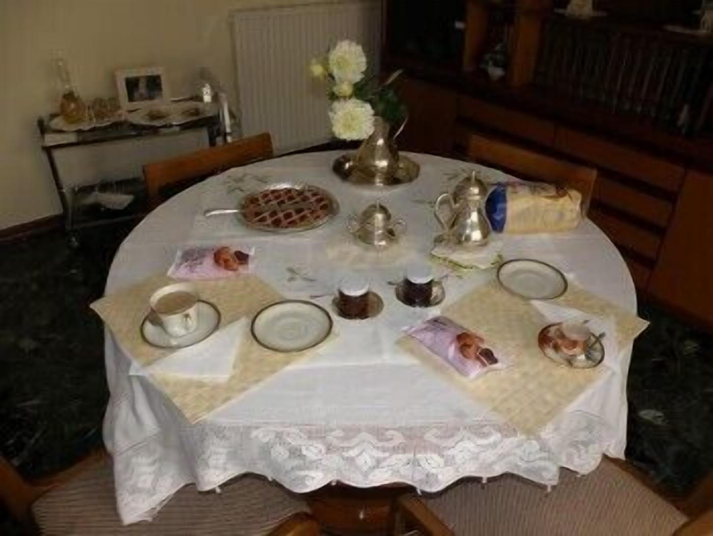 A round dining table with a lace tablecloth, surrounded by chairs.