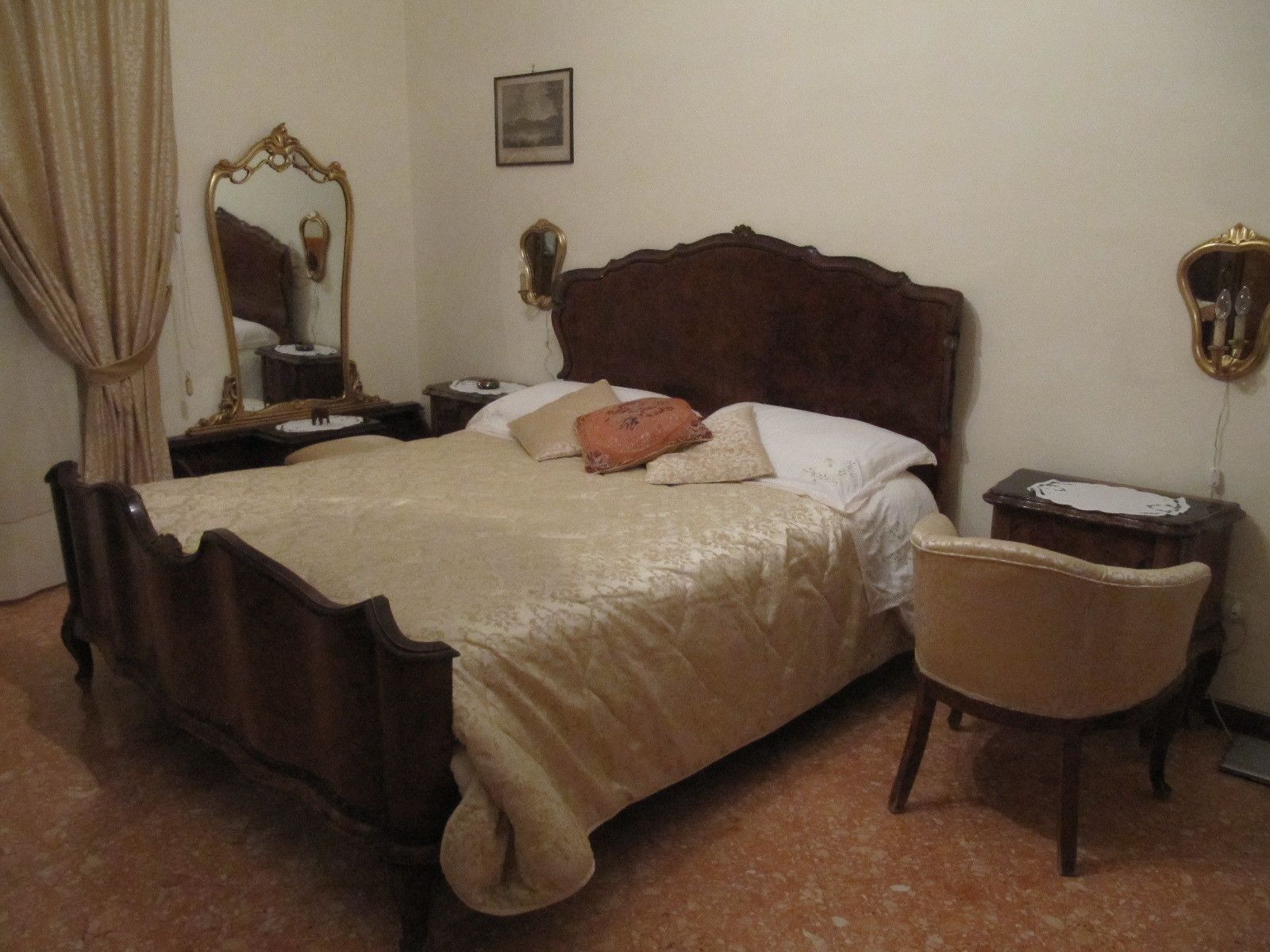 Een slaapkamer met een houten bed, een stoel, een nachtkastje en een spiegel.