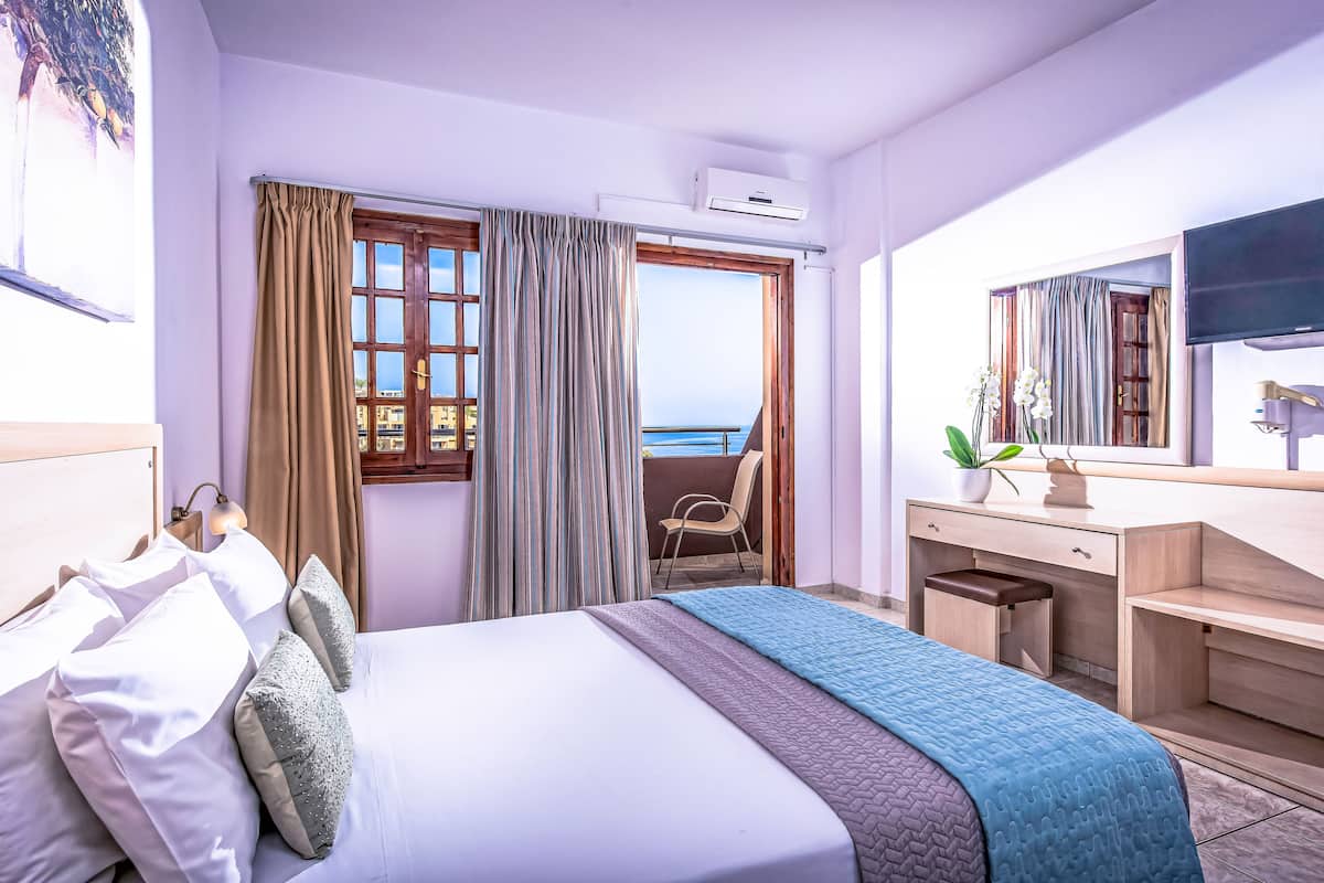 A hotel room with a bed, a desk, a chair, a TV, and a window with curtains.