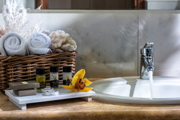 A bathroom vanity with a white sink, a wicker basket containing rolled towels, toiletries, and a yellow flower.