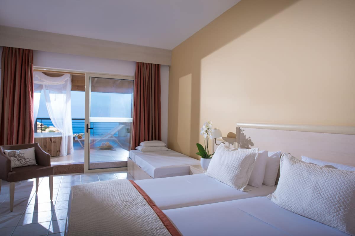 A hotel room with two beds, a balcony with a view of the sea, a chair, and a potted plant.
