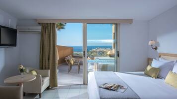 Quarto de hotel com uma cama, uma mesinha, uma cadeira, uma televisão e vista para o mar.