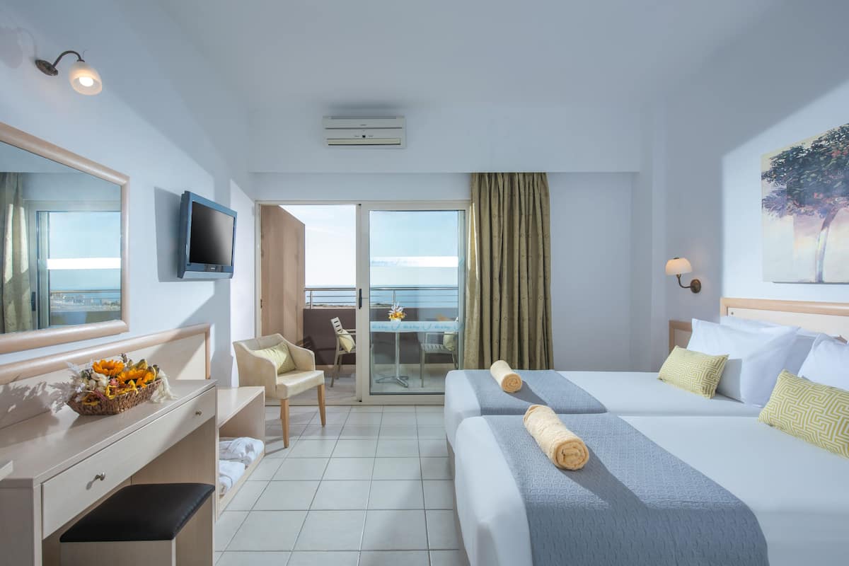 A hotel room with two beds, a desk, a chair, a TV, and a balcony with a view.