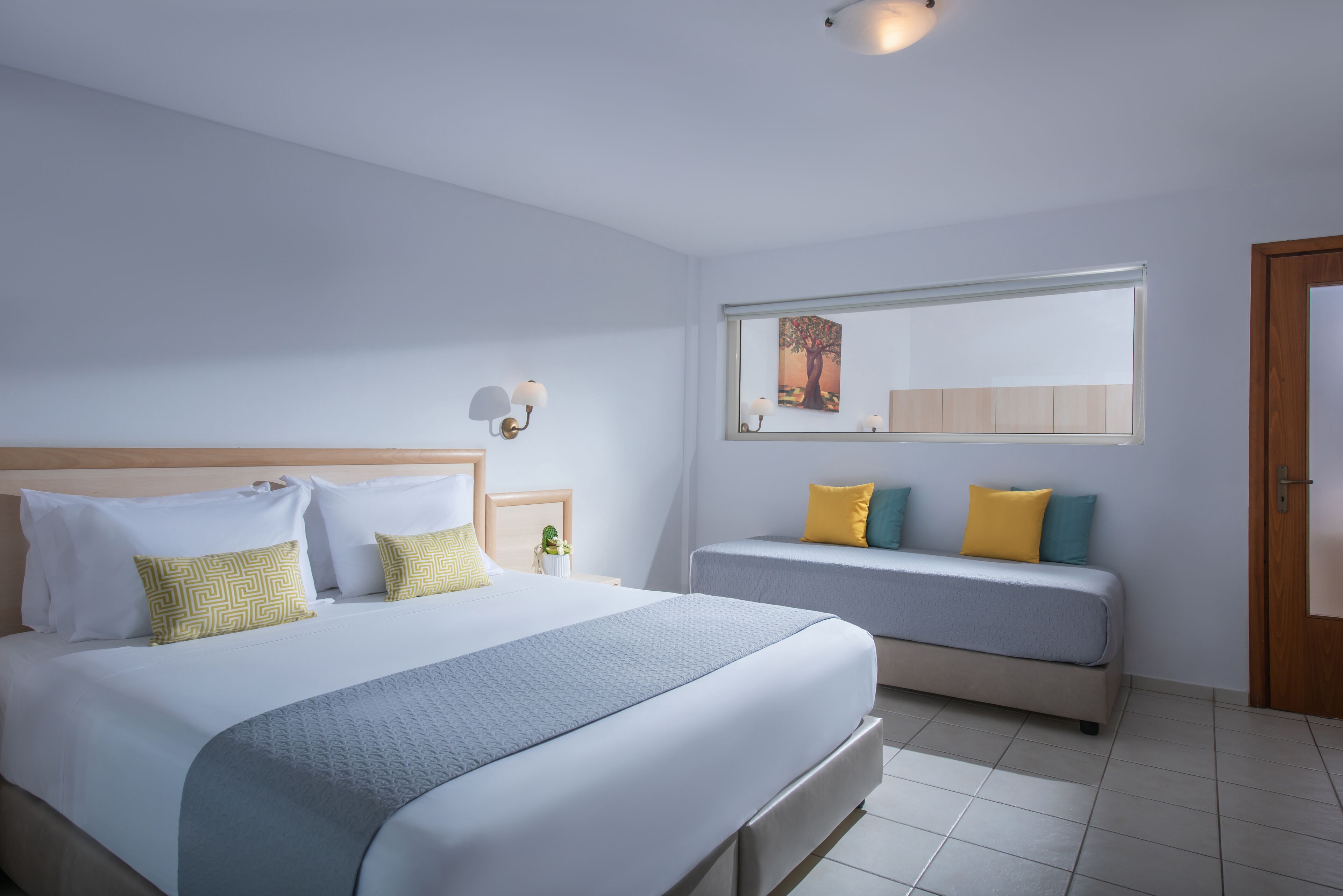 Una habitación de hotel con una cama grande, una cama más pequeña, una mesita de noche, un espejo y una ventana.