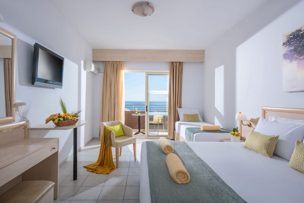 A hotel room with a bed, a desk, a chair, a television, and a balcony with a view of the sea.