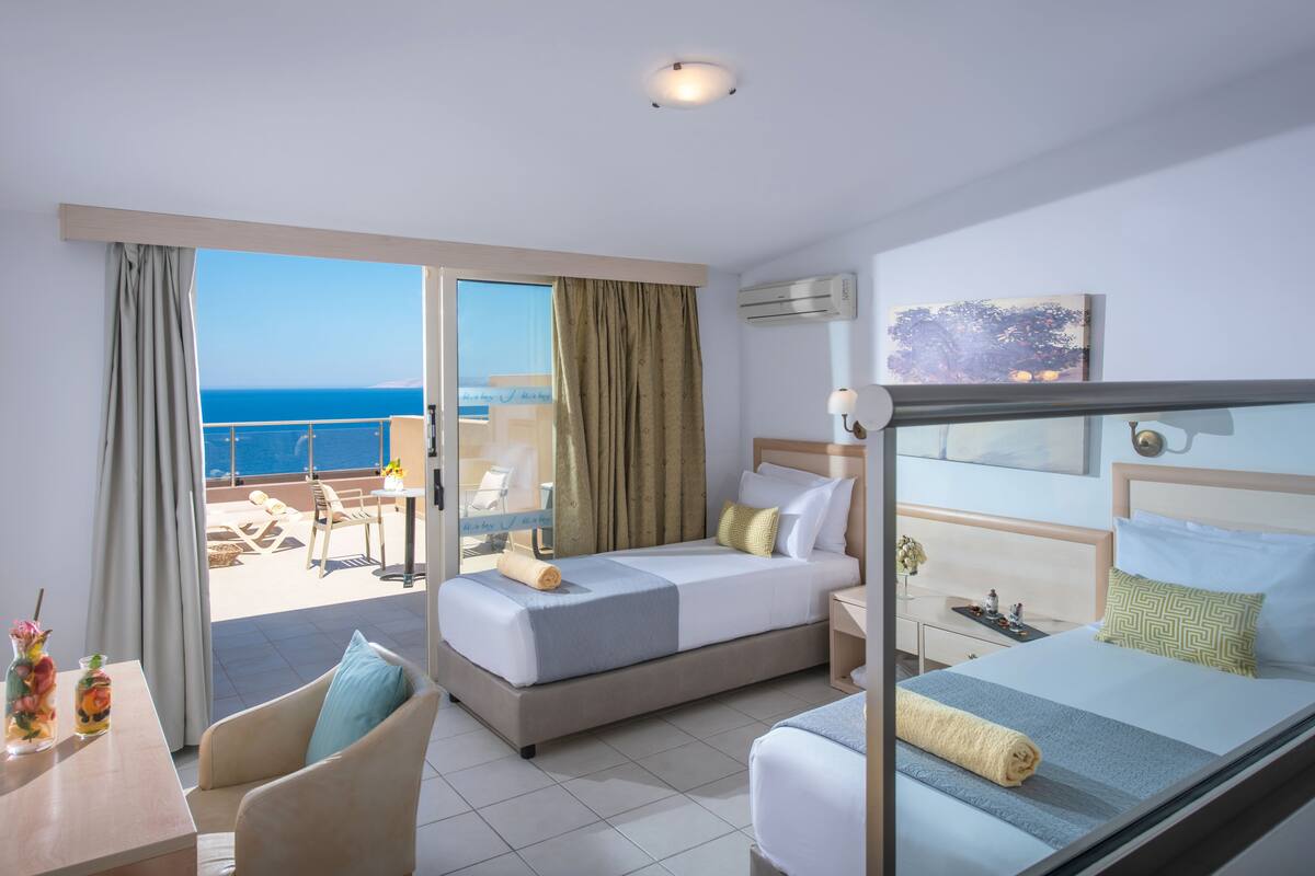 A hotel room with a balcony, a bed, a chair, a table, and a desk.