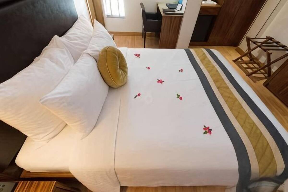 A bed with white linens, a green pillow, and a striped bedspread.