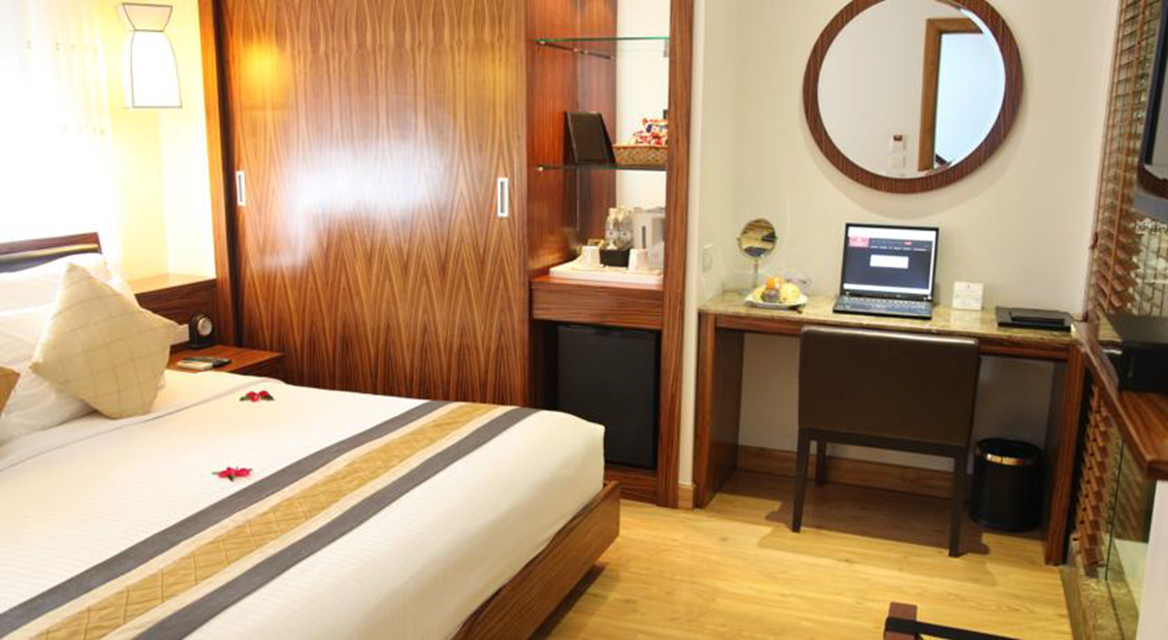 Ein Hotelzimmer mit einem Bett, einem Schreibtisch mit Laptop, einem Spiegel und einer kleinen Mülleimer.