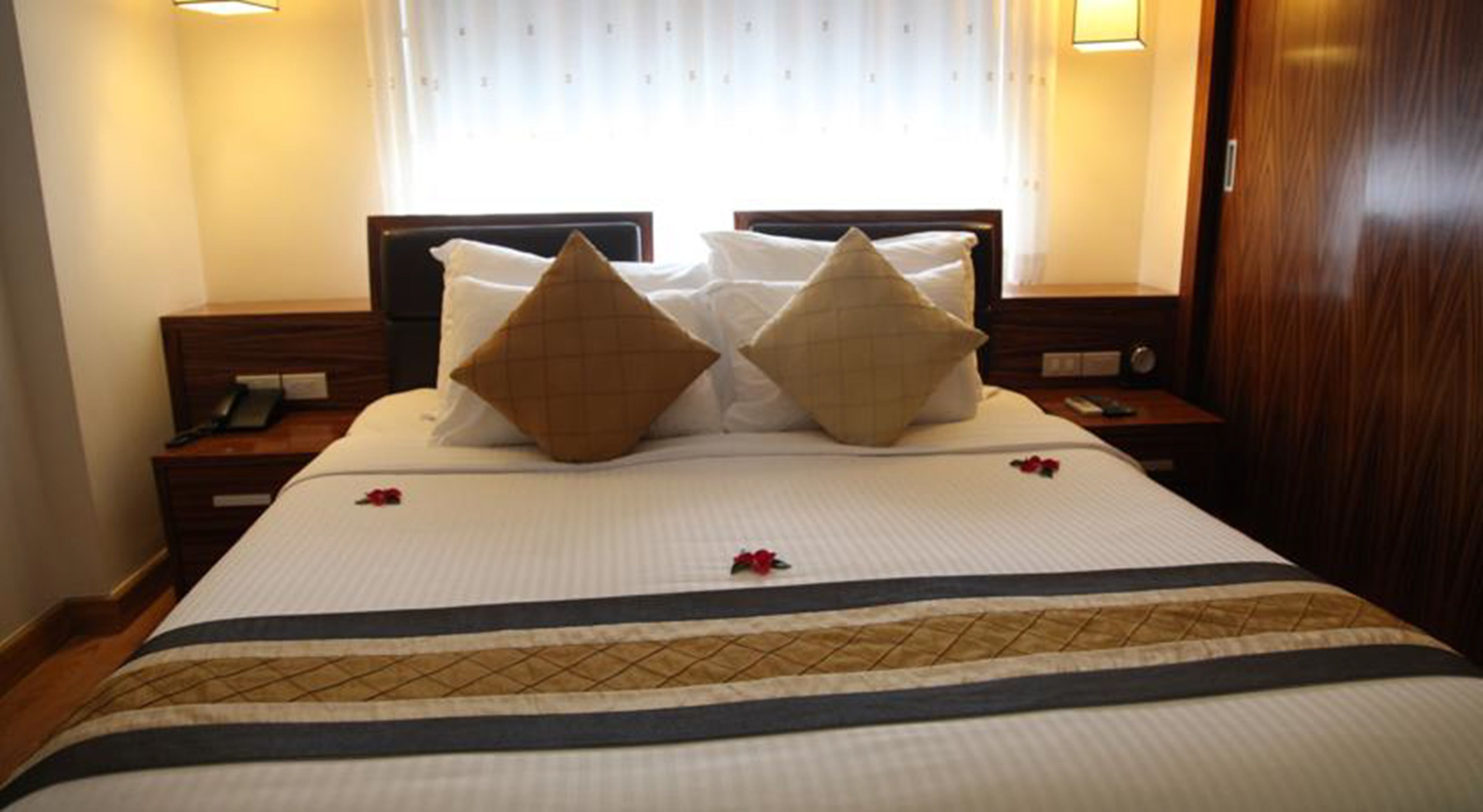 Un lit bien fait, avec une couvre-lit à rayures, deux coussins décoratifs et une petite fleur rouge posée sur le lit.