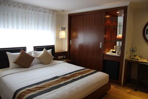 A hotel room with a large bed, wooden wardrobe, bedside table, and a small desk with a mirror.