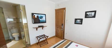 A modern bedroom with a large bed, a television, a wooden door, and a small shelf.