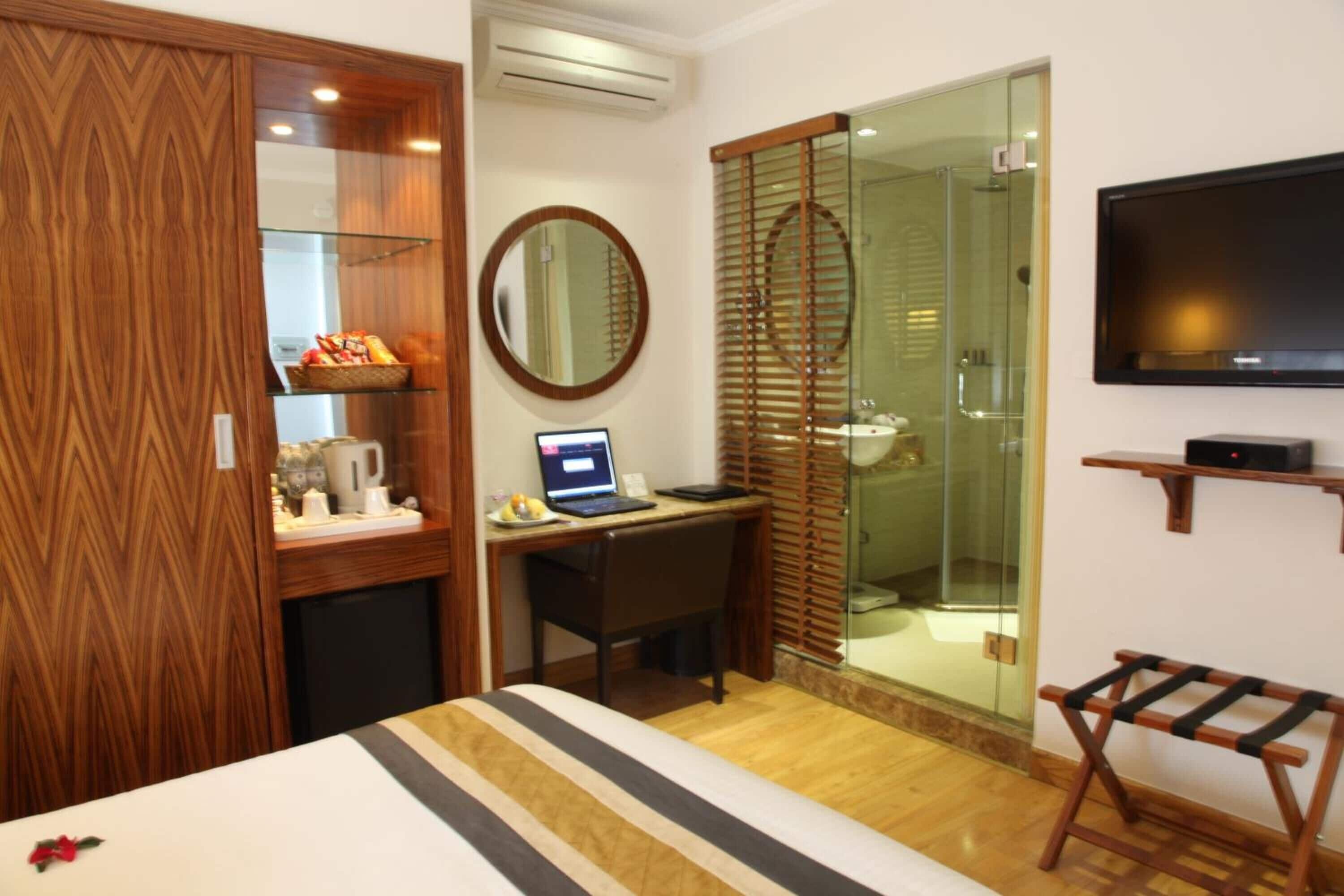 Une chambre d’hôtel comprenant un lit, un bureau avec un ordinateur portable, une télévision, une douche et une armoire en bois.