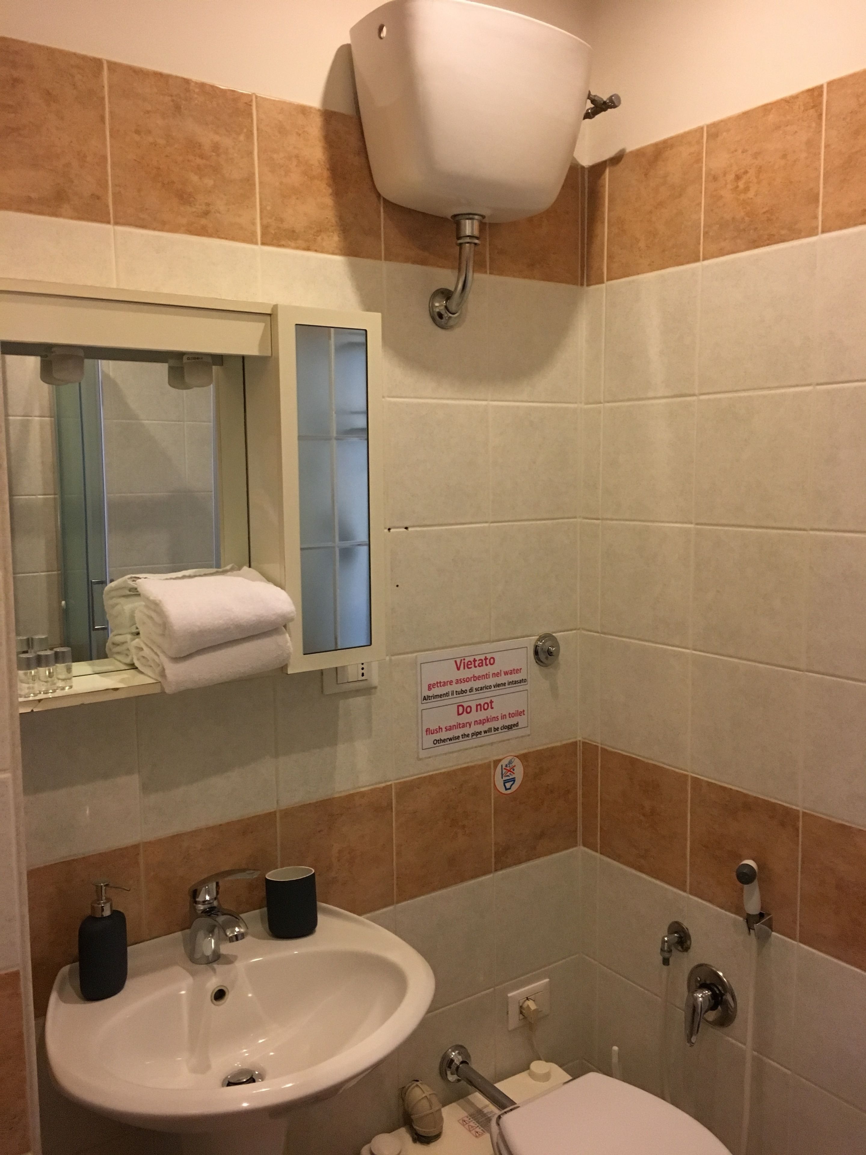 A bathroom with a sink, mirror, towel rack, toilet, and a sign instructing not to flush sanitary napkins.