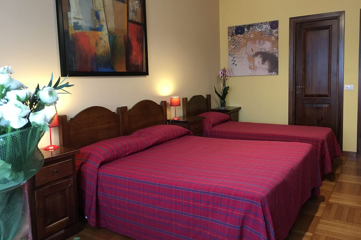 A room with two beds, a wooden headboard, a painting, a door, and a nightstand with a lamp.