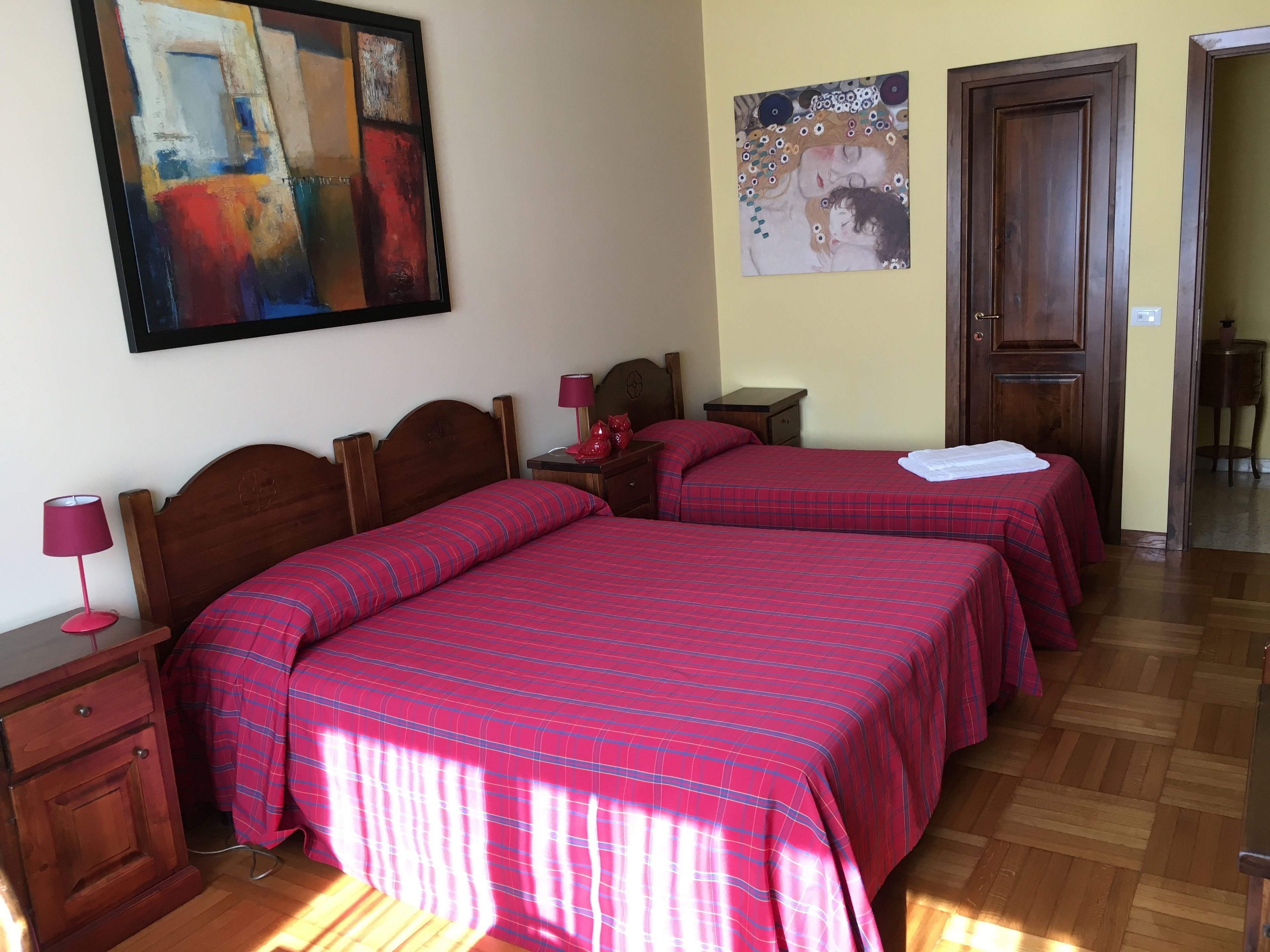 A hotel room with two beds, wooden headboards, a nightstand with a lamp, and artwork on the walls.