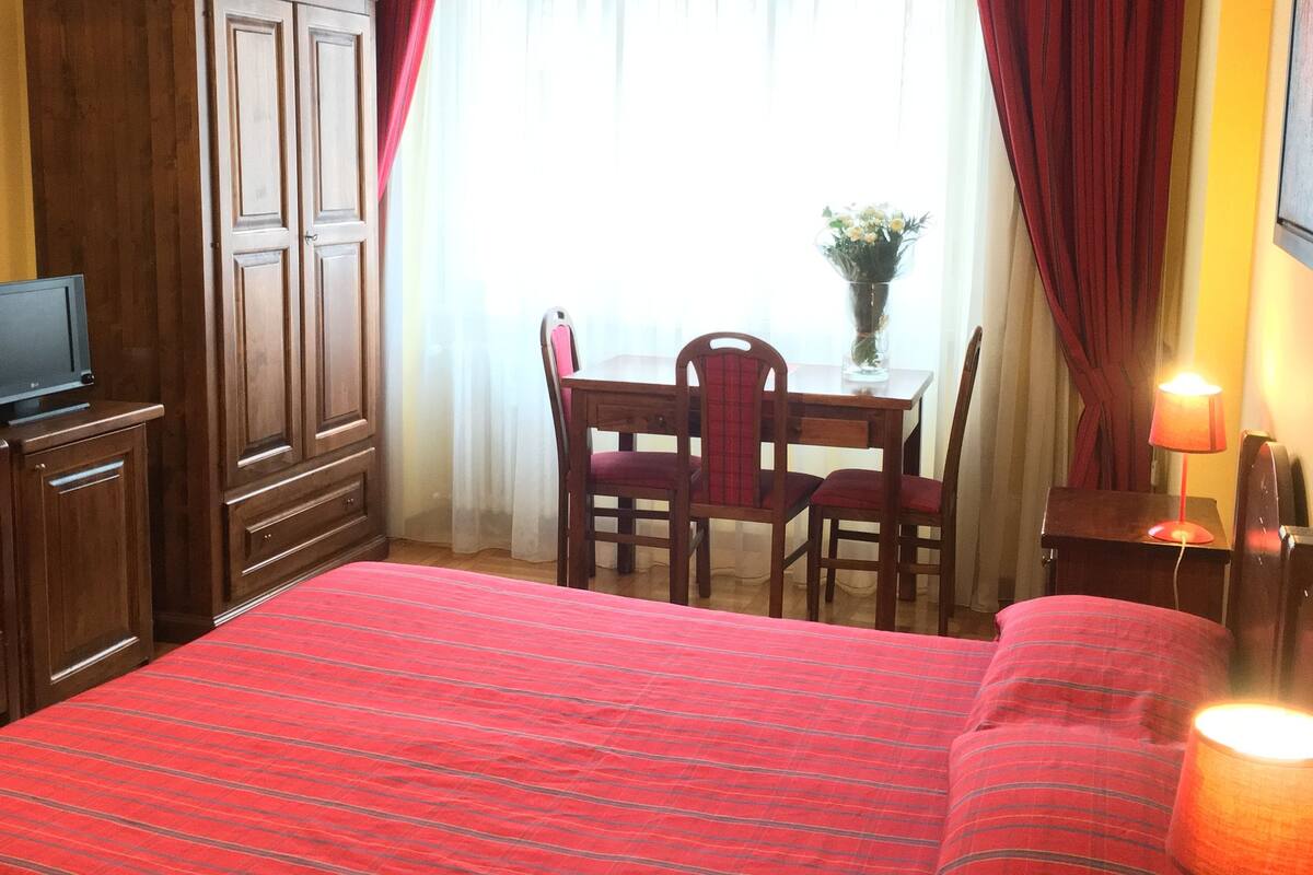 A hotel room with a bed, a desk, a chair, a TV, and a lamp.