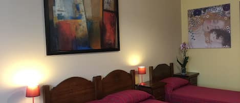 A hotel room with two beds, a nightstand with a lamp, and two wall-mounted paintings.