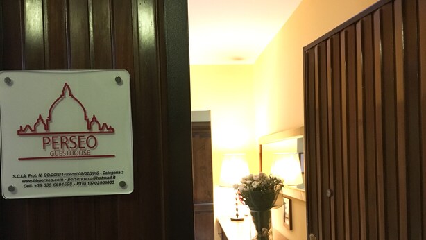A sign for Perseo Guesthouse with contact details and a reception area with a lamp and a vase of flowers. - Perseo B&B (Rome)