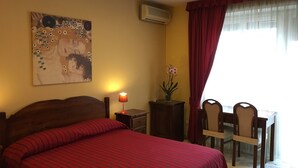 A hotel room with a bed, a desk, chairs, a lamp, an air conditioner, and a painting on the wall. - Perseo B&B (Rome)