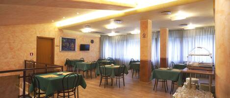 A dining area with multiple tables and chairs, a buffet station, and a clock on the wall.