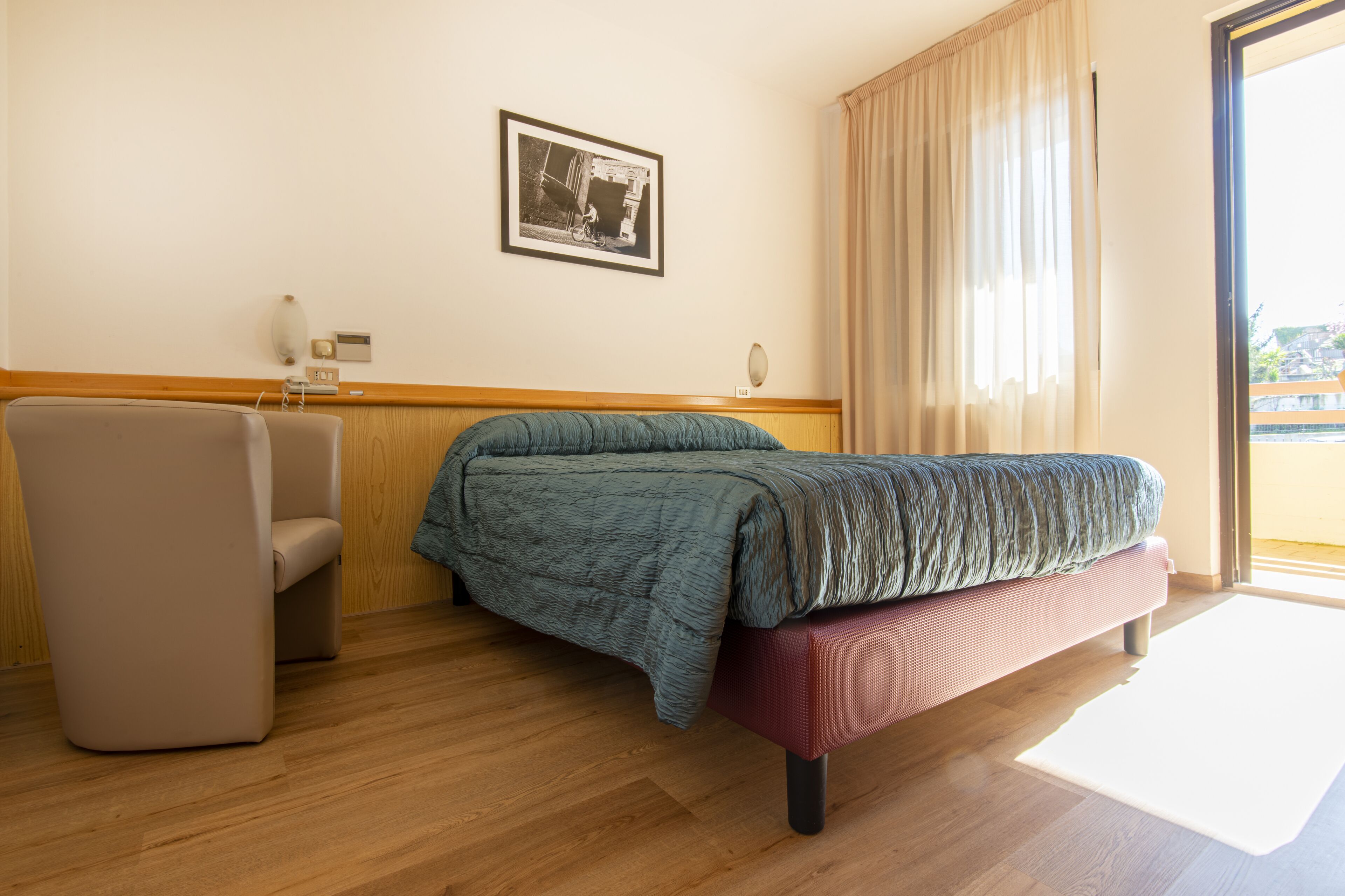 Una habitación de hotel con una cama, una silla, una mesita y un cuadro en la pared.