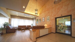 A spacious living area with a sofa set, a coffee table, and a lamp. There is a large window with curtains, a potted plant, and a framed picture on the wall. - Pennile (Ascoli Piceno)