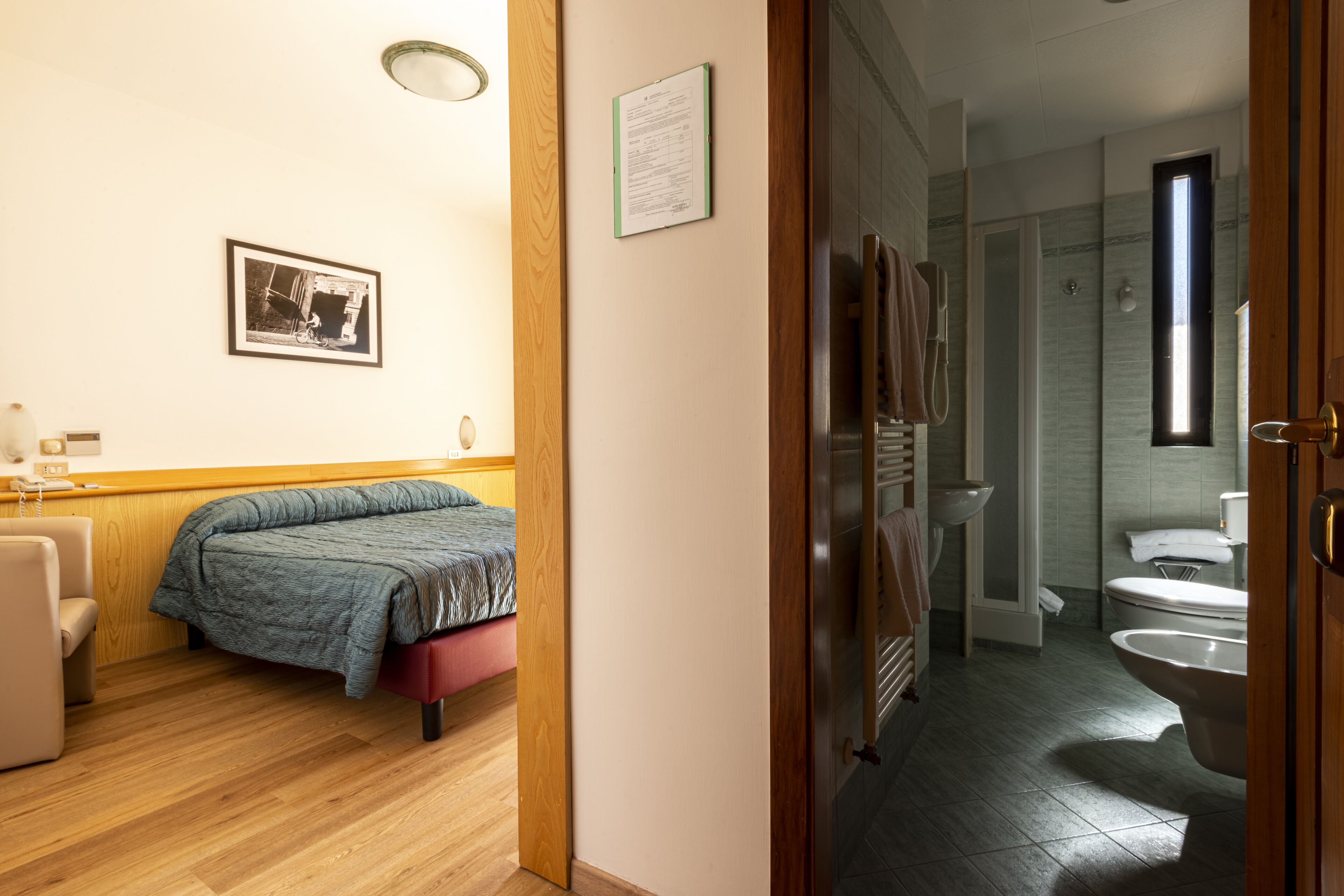 A bedroom with a bed, a chair, a bedside table, and a framed picture on the wall.