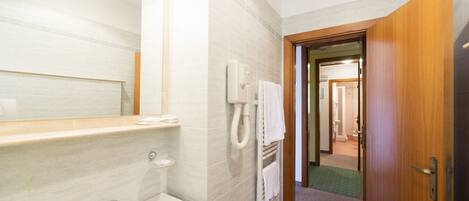 A bathroom with a sink, mirror, towel dispenser, and a wooden door leading to another room.