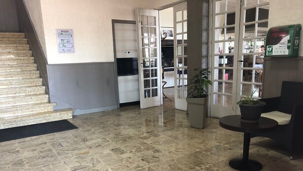 Um hall com piso de mármore, escada, balcão de recepção e um vaso de planta.