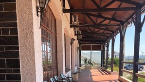 Uma área de estar coberta ao ar livre com ladrilhos de terracota, vasos de pedra com flores e vista para a paisagem.