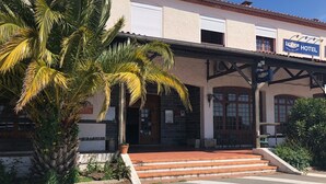 Um hotel com fachada tradicional, uma palmeira em frente e uma placa indicando que é um hotel.