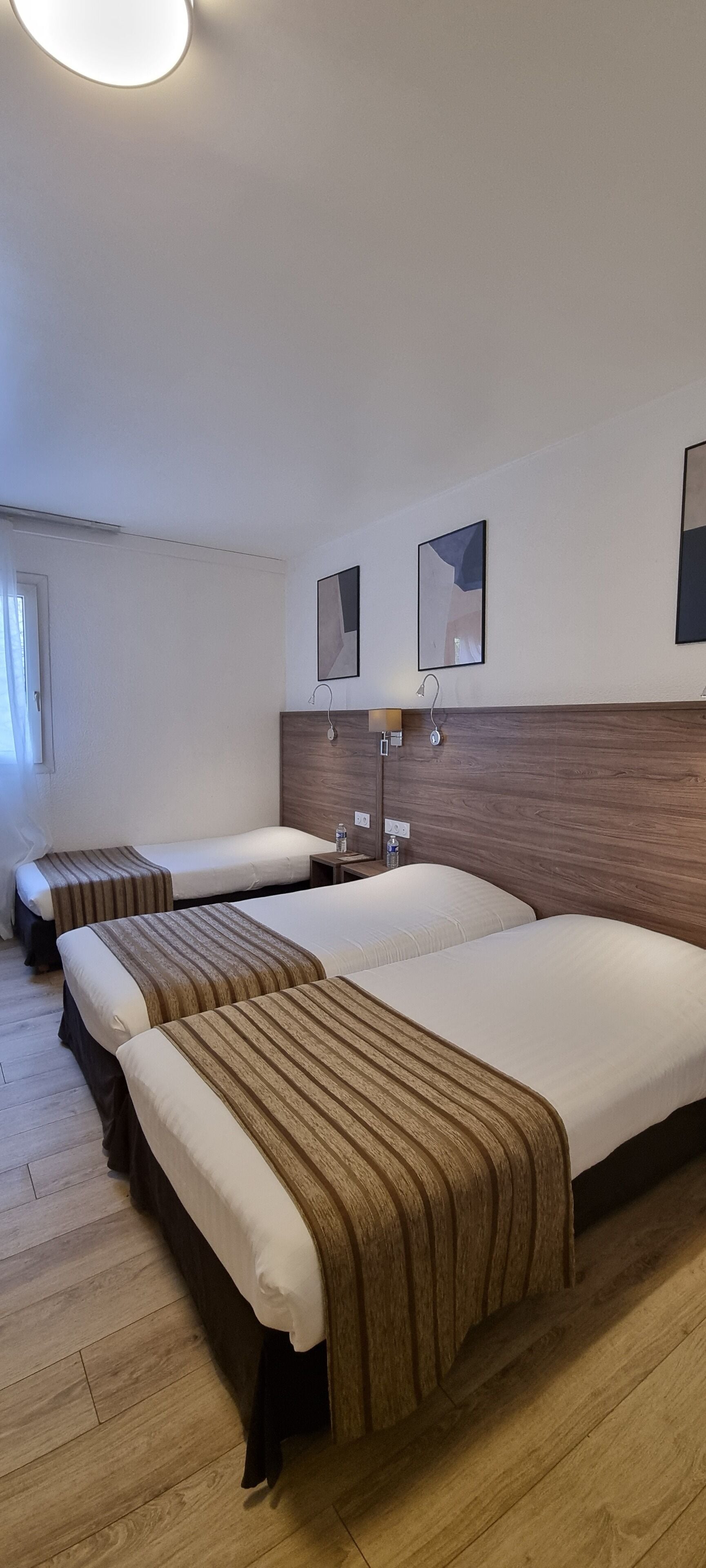 A hotel room with two beds, wooden headboard, bedside tables, and wall-mounted mirrors.