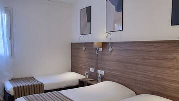 A hotel room with two beds, wooden headboard, bedside tables, and wall-mounted mirrors.