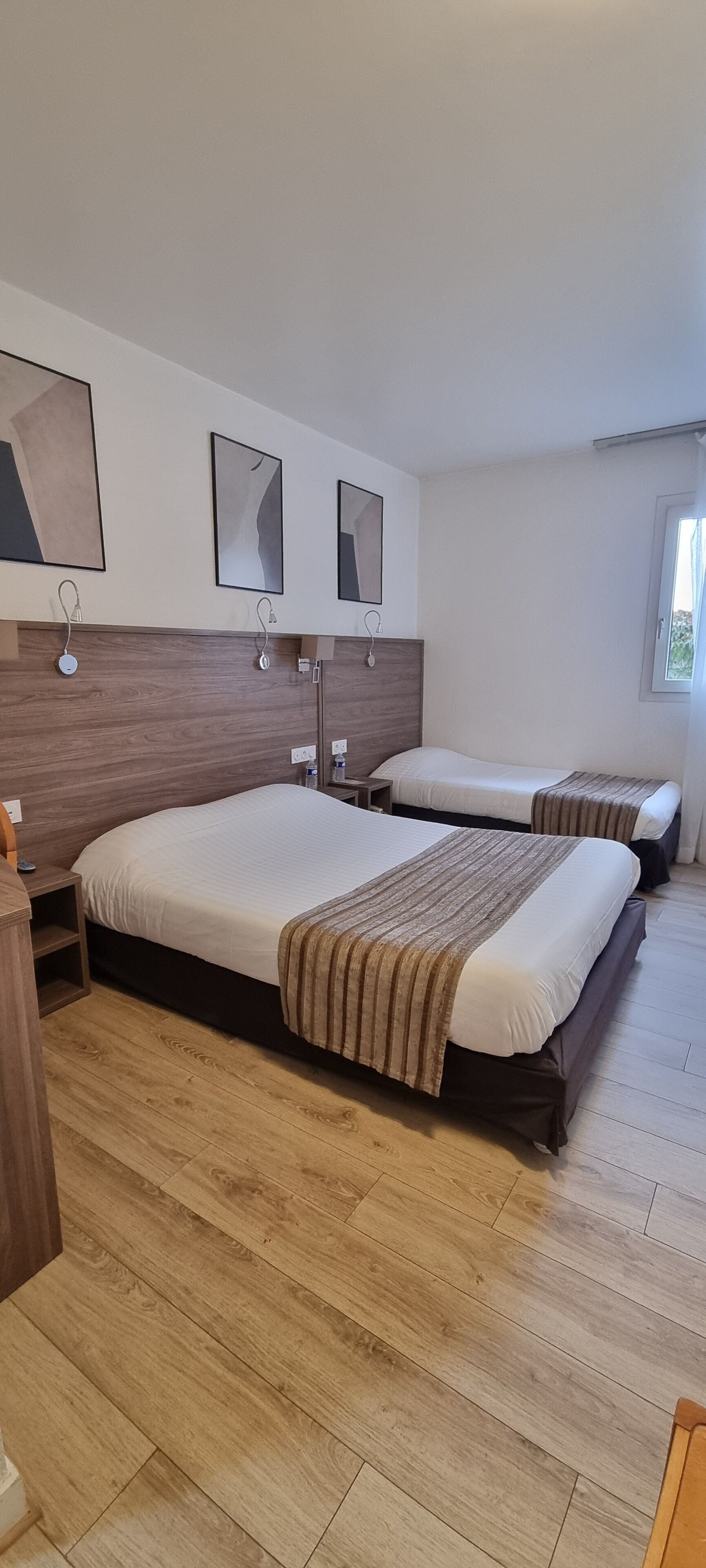 A hotel room with two beds, wooden flooring, and a window.
