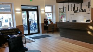 Un área de recepción moderna con un cartel que dice 'Welcome', piso de madera, sillas tapizadas en negro y una mesa de recepción.