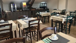 Un restaurante con varias mesas, sillas y una zona de cocina al fondo.