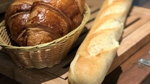 Una mesa de madera con una cesta de cruasanes y una baguette.