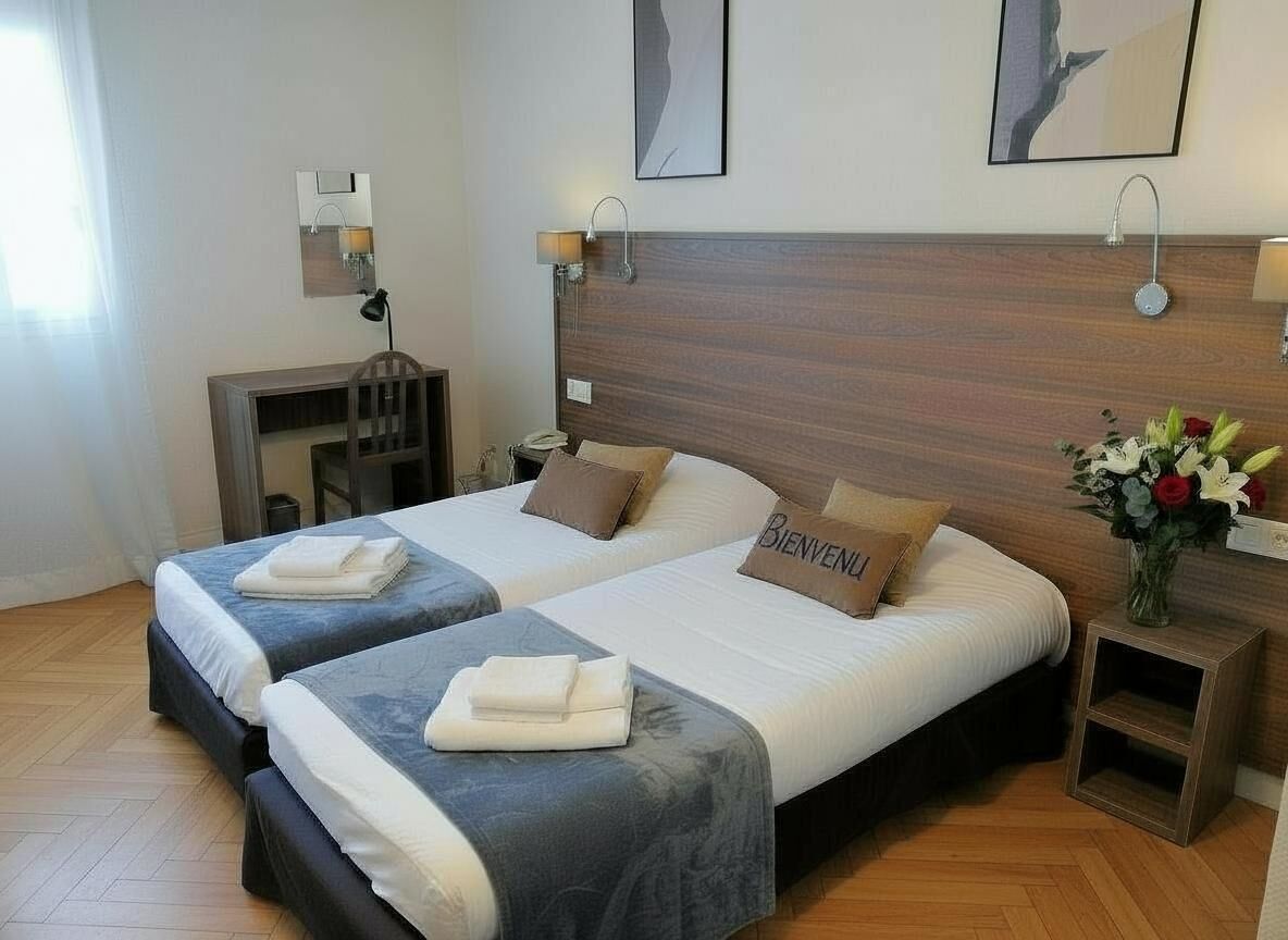A hotel room with two beds, a wooden headboard, bedside lamps, a small table, and a vase with flowers.