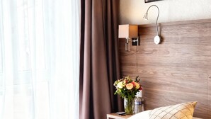 Una cama bien hecha con un cartel de bienvenida, una mesita de noche con un jarrón de flores y una lámpara de pared.