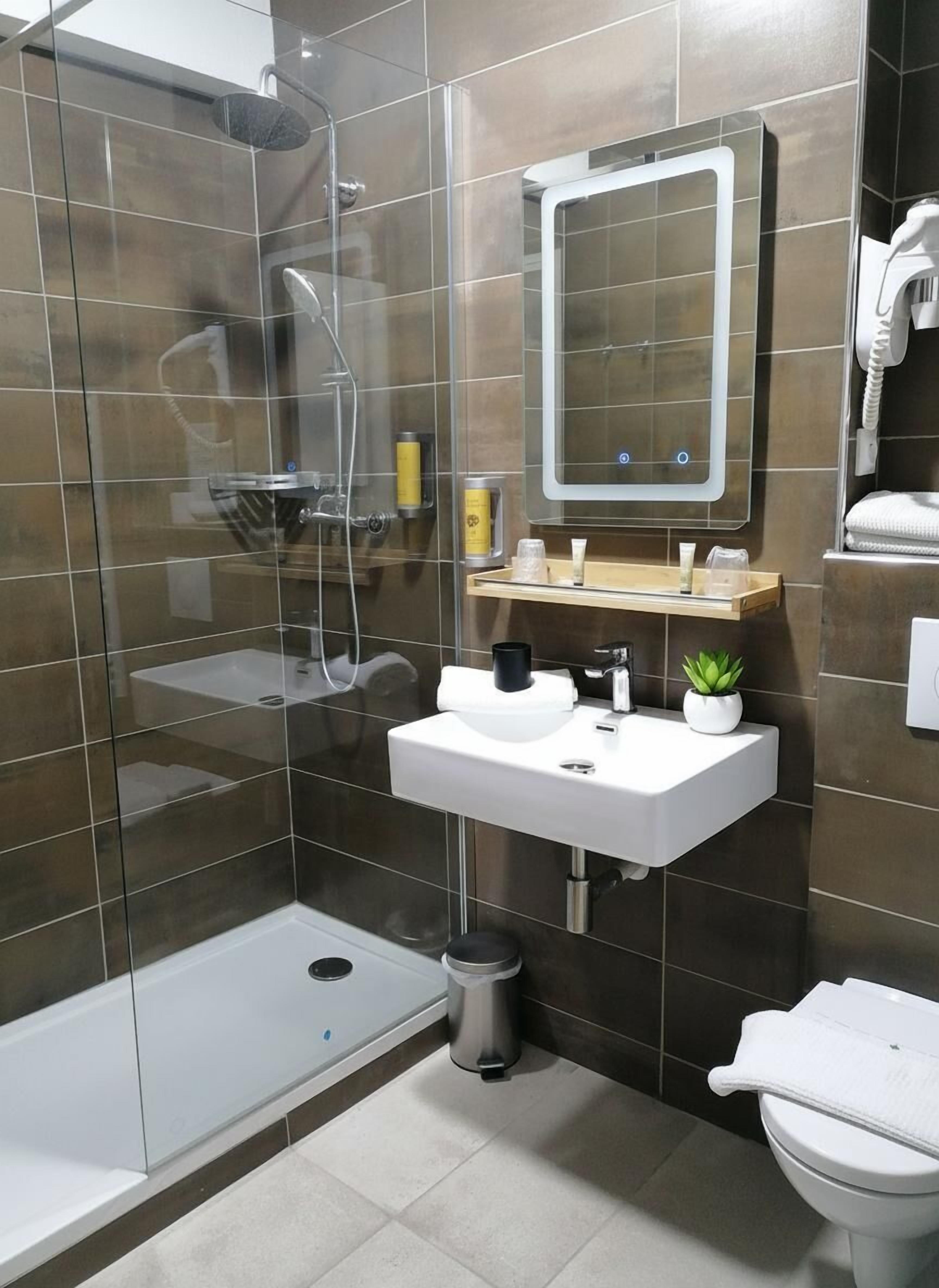 Een moderne badkamer met een douchecabine van glas, een witte wastafel met spiegel erboven en een toilet.