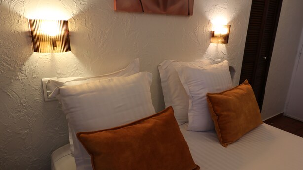 A hotel room with a bed, white pillows, and two wall-mounted lights. - Hotel Villa Roseraie (Vence)