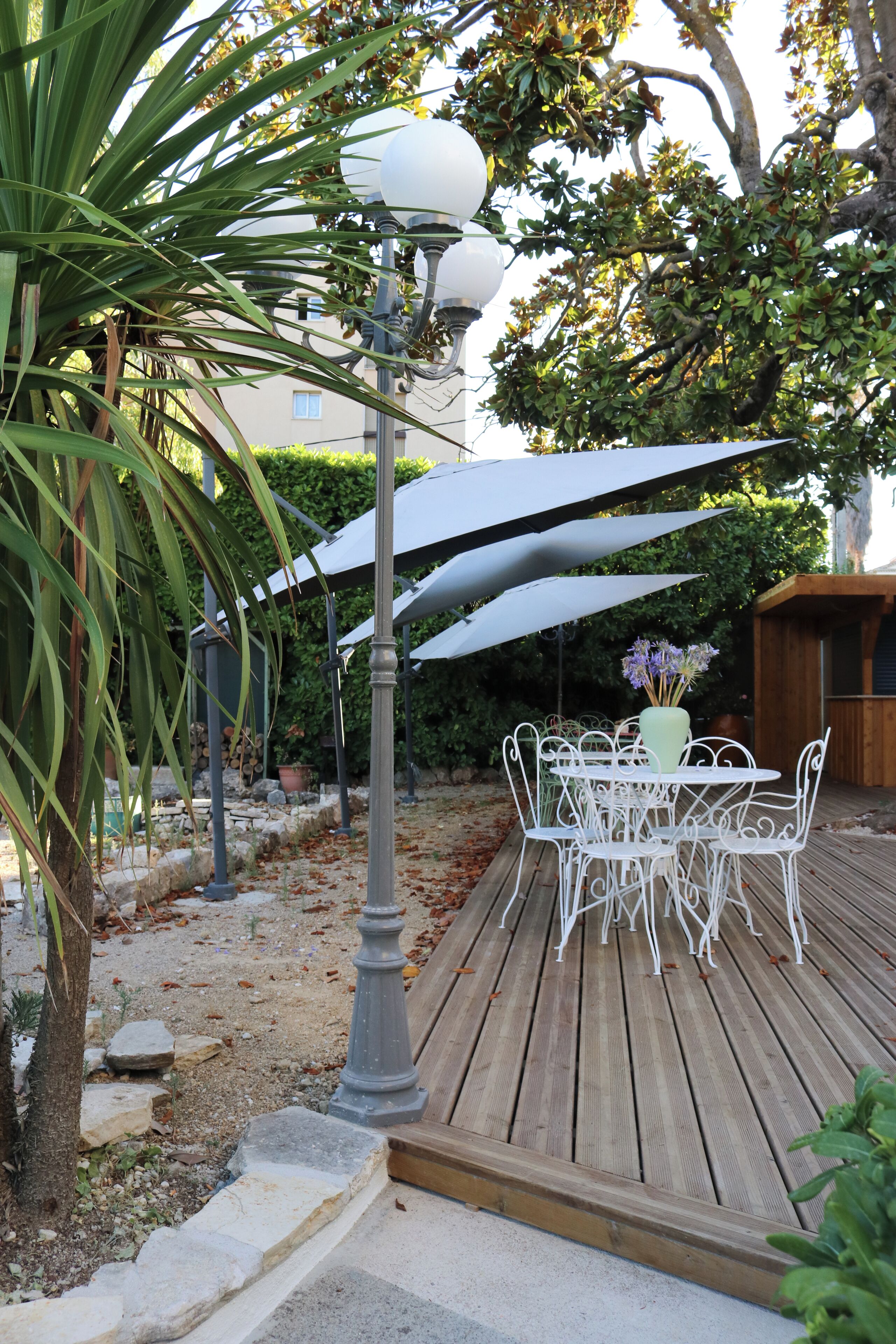 A wooden deck with outdoor furniture, including a table and chairs, surrounded by umbrellas and a street lamp.