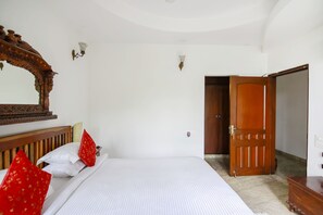 A hotel room with a large bed, a wooden headboard, a mirror, and a door leading to another room.