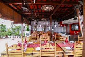 A restaurant with wooden tables and chairs, red tablecloths, and hanging lanterns.