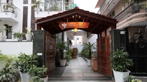 Uma viela estreita com plantas em vasos de ambos os lados, levando a uma entrada de edifício com um arco de madeira e uma placa acima.