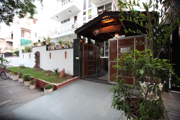 A building entrance with a wooden archway, potted plants, and a sign reading "Ombi Home".