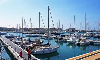 Un puerto deportivo con numerosas embarcaciones amarradas, un muelle y edificios al fondo.