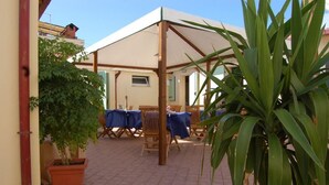 An outdoor patio area with a covered seating area, potted plants, and a tiled floor. - La Papaya (Pisa)